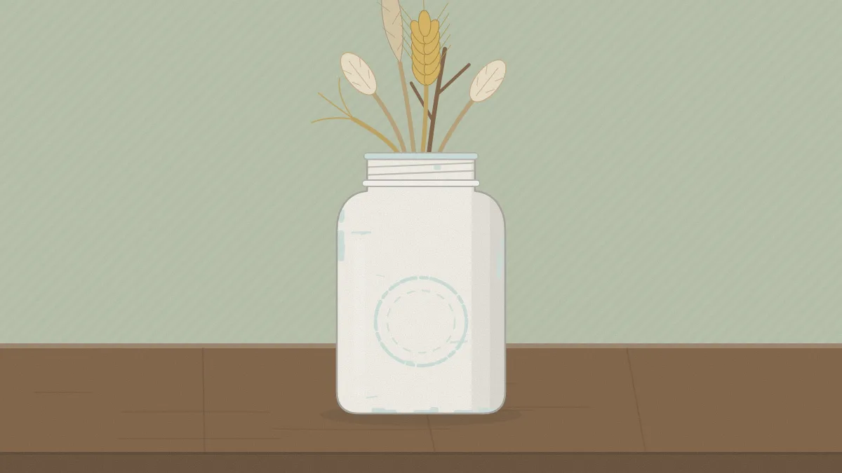 A white painted mason jar with raised lettering and rim sanded back to show glass, holding a few dried stems