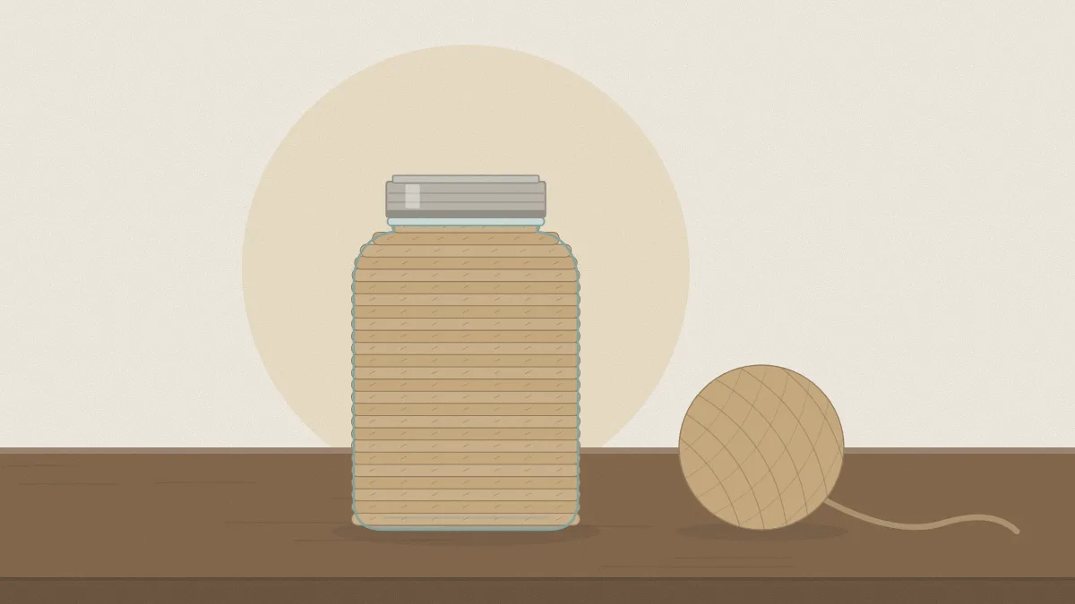 A clear pint mason jar wrapped in neat rows of jute twine from base to shoulder, with a ball of twine beside it